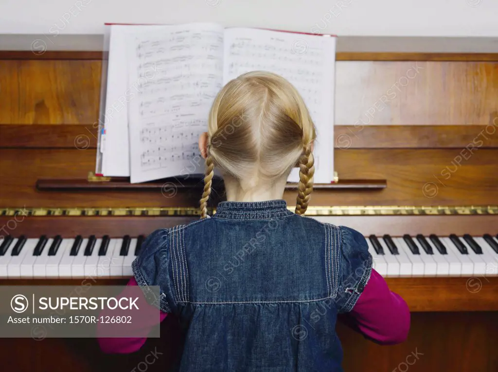 A little girl playing a piano, rear view, portrait