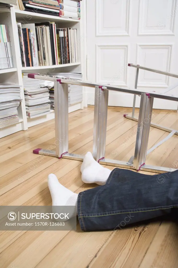 Human legs lying next to a ladder on its side