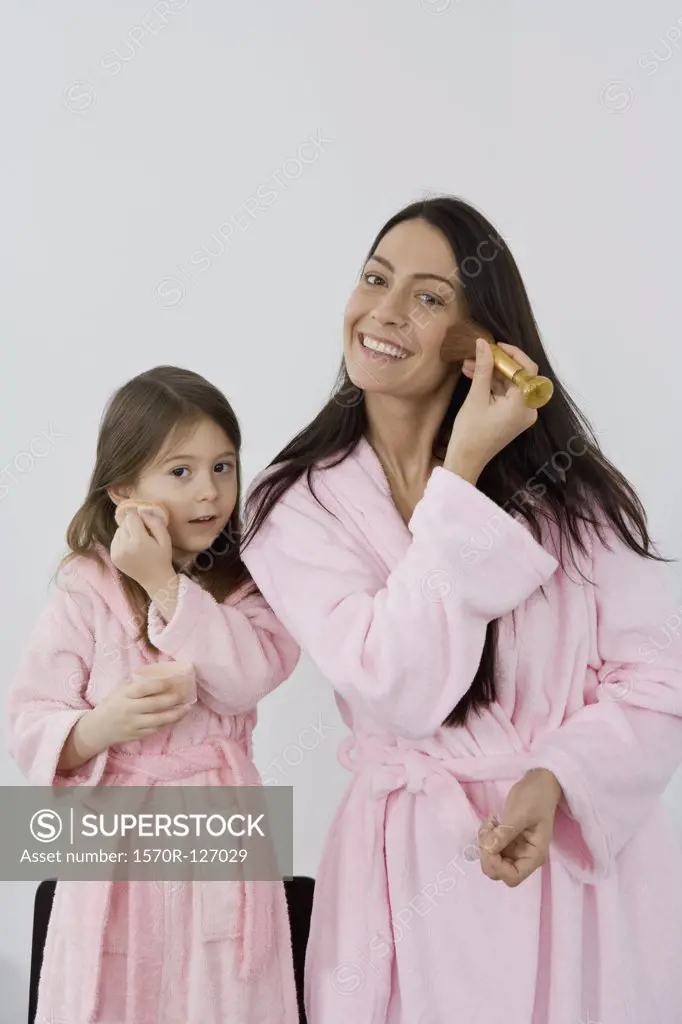 A mother and daughter in pink bathrobes applying make up