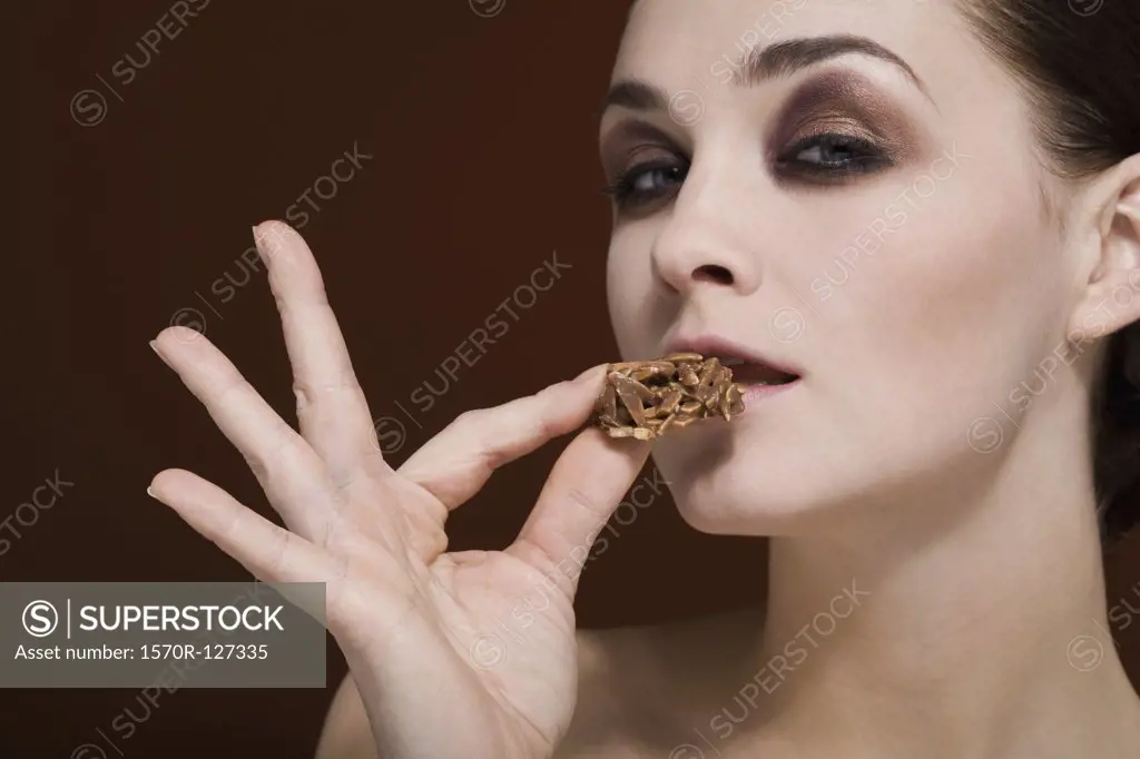 A woman holding an almond chocolate cluster to her mouth
