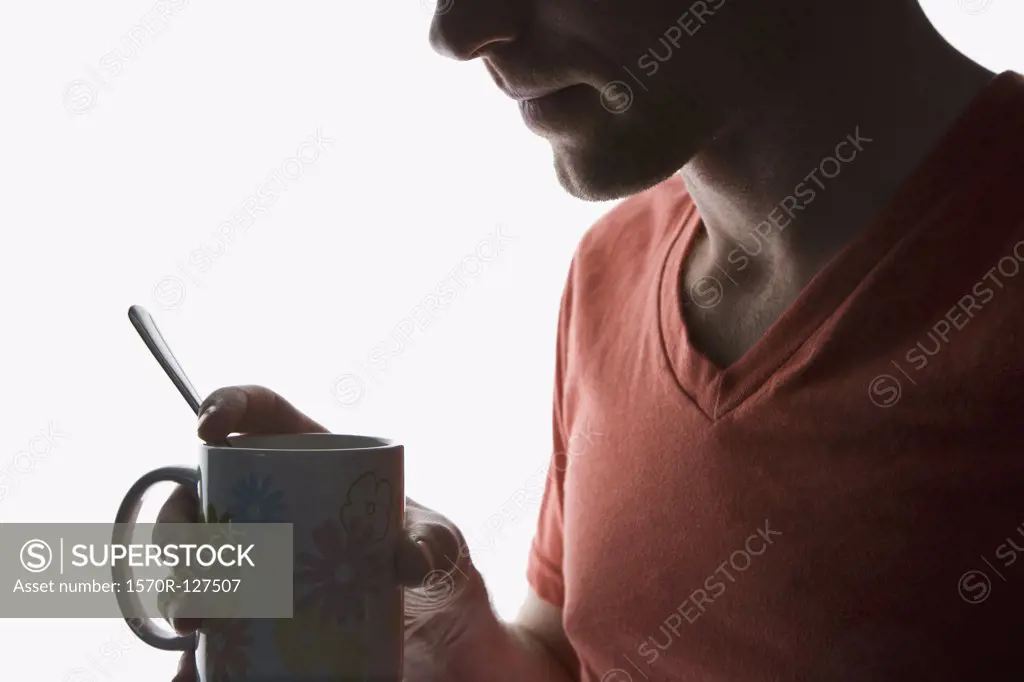 A man with a cup of coffee, back lit, obscured face