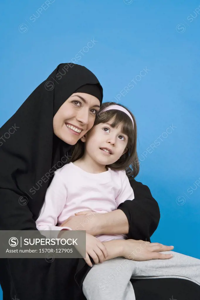 A woman wearing a Hijab and holding her daughter on her lap