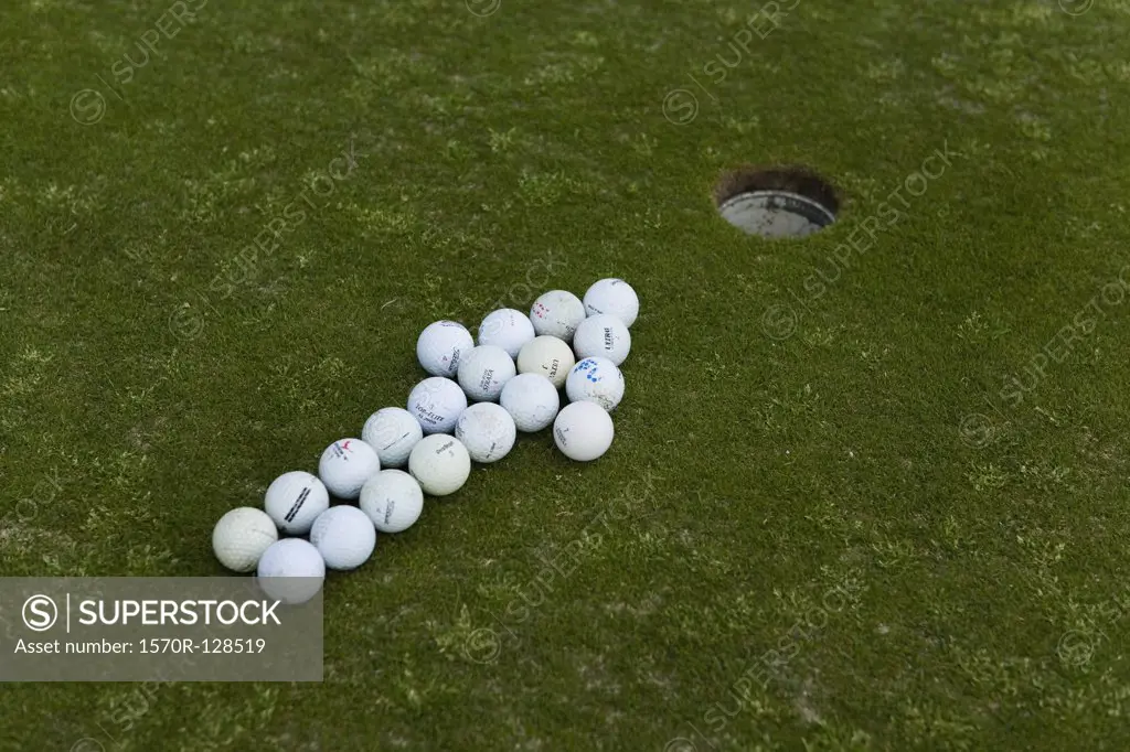Arrow of golf balls pointing to a hole on a putting green