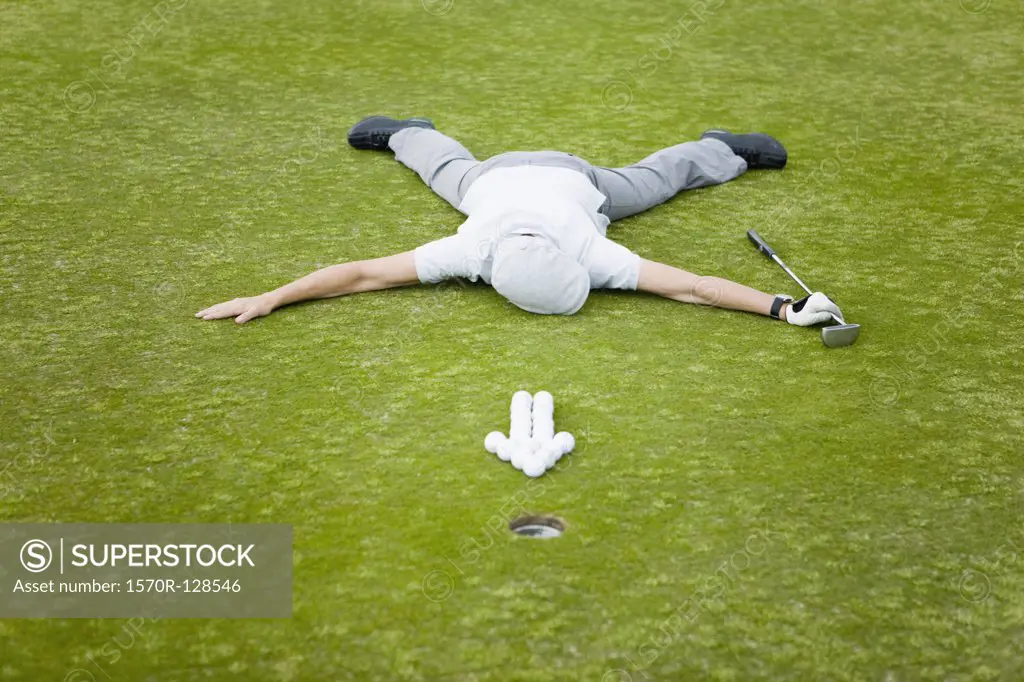 A golfer lying on a putting green behind an arrow of golf balls
