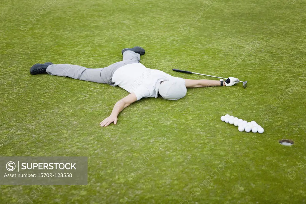 A golfer lying on a putting green behind an arrow of golf balls