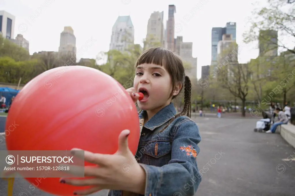 A young girl blowing up a balloon in Central Park, New York City