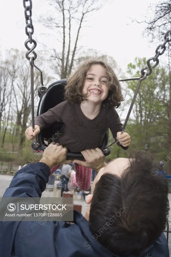 A father pushing his daughter on a swing in a park