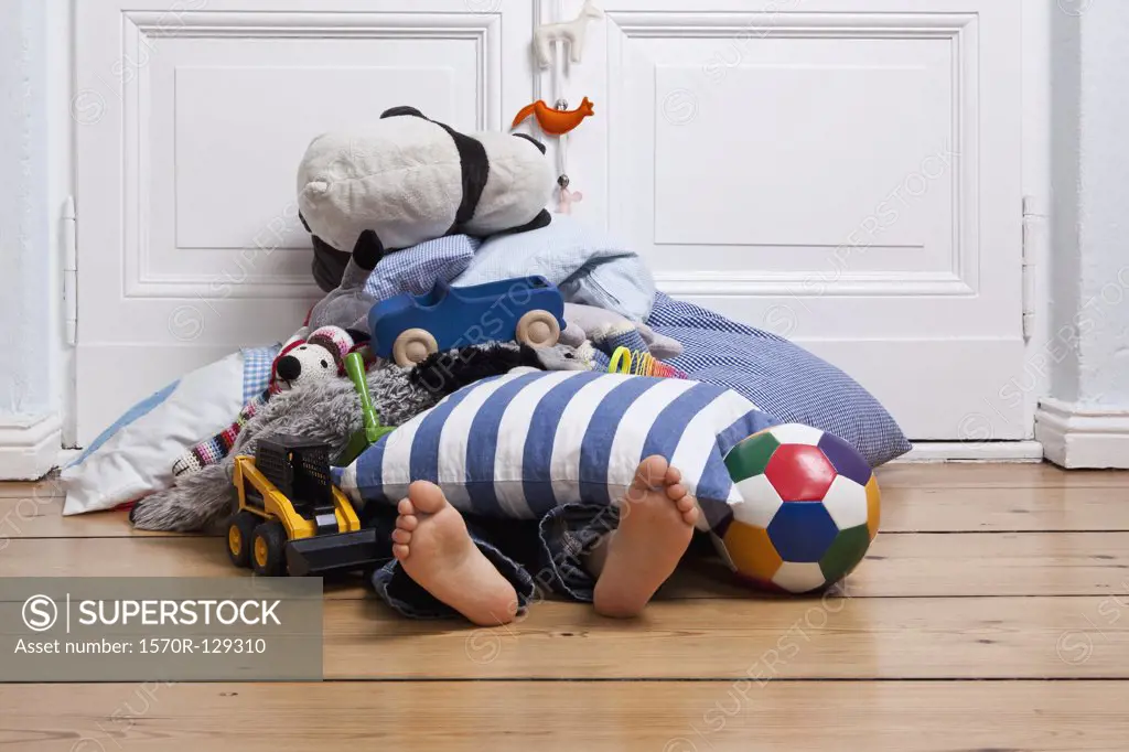 A child covered in toys, only feet visible