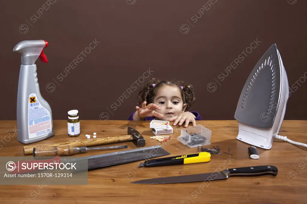 A young girl reaching onto a table of dangerous objects, studio shot