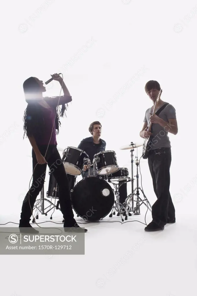 A drummer, guitarist and singer performing, studio shot, white background, back lit