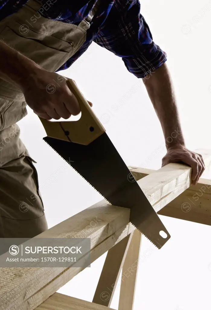 A carpenter sawing a wooden plank, focus on saw