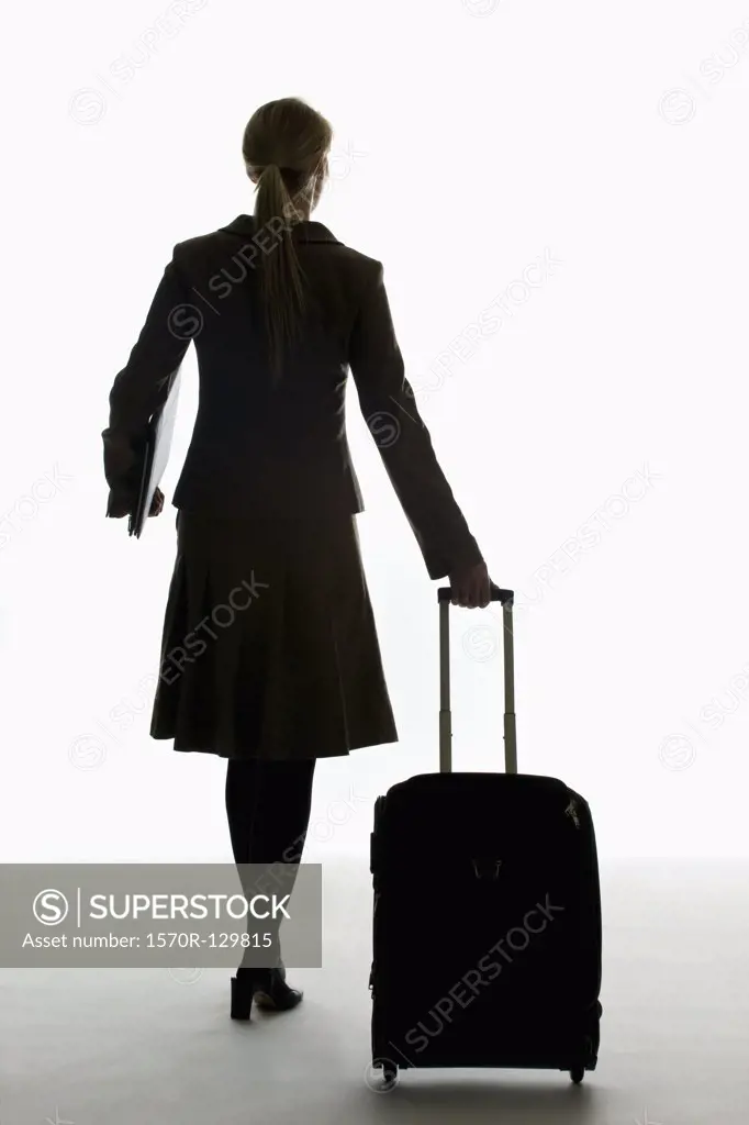 A businesswoman pulling a wheeled carry on and holding a portfolio