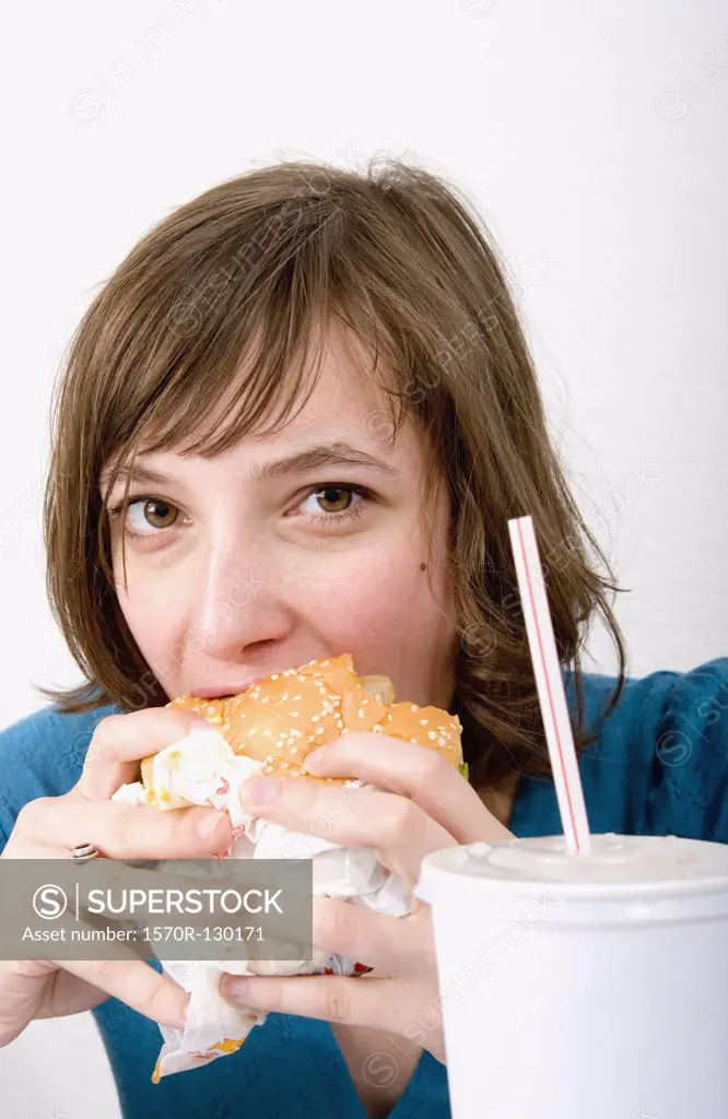 Young woman eating a burger and drinking soda