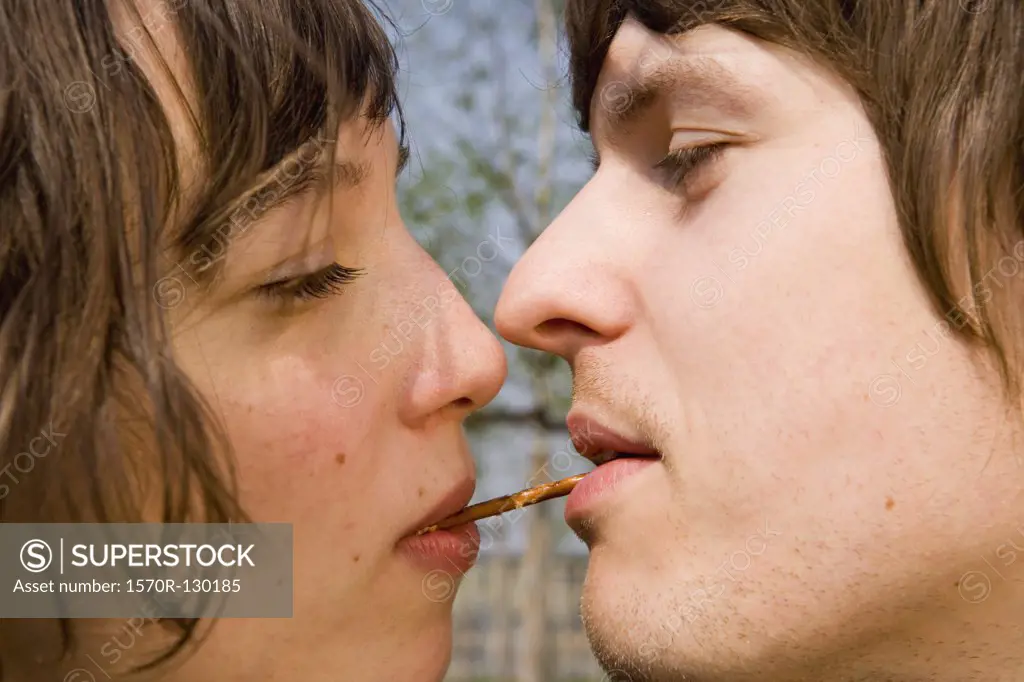Young couple sharing a pretzel between their mouths