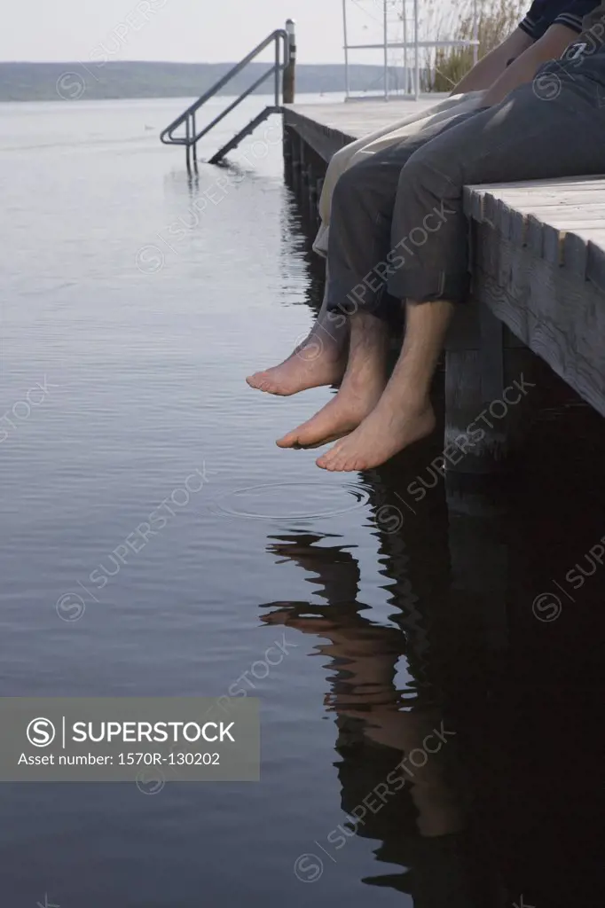 Two men sitting on jetty by lake