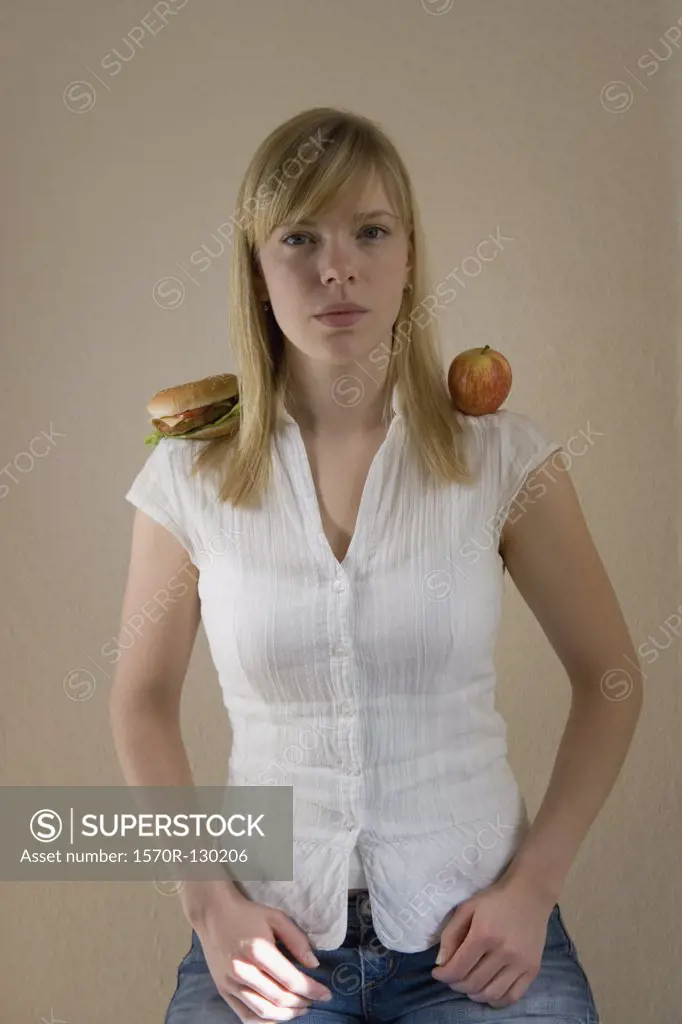 Young woman sitting with a hamburger on one shoulder and an apple on the other