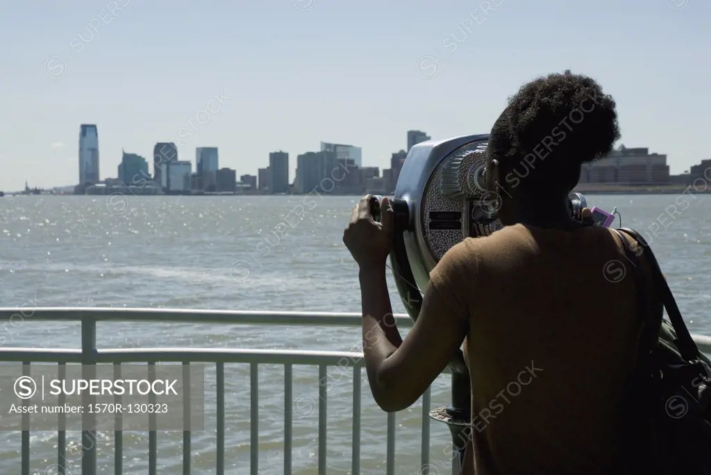 A woman looking at a city skyline through coin operated binoculars