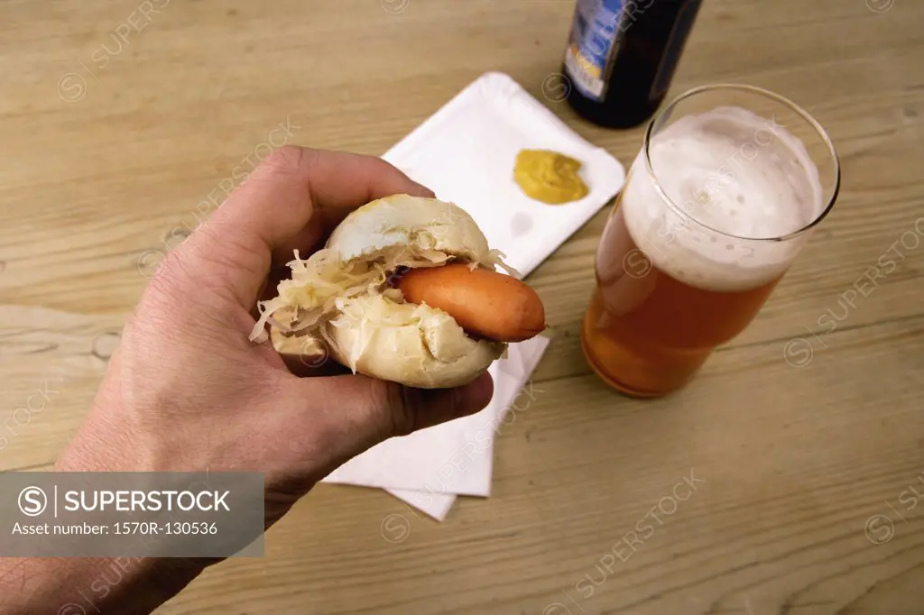 Man holding hot dog above glass of beer