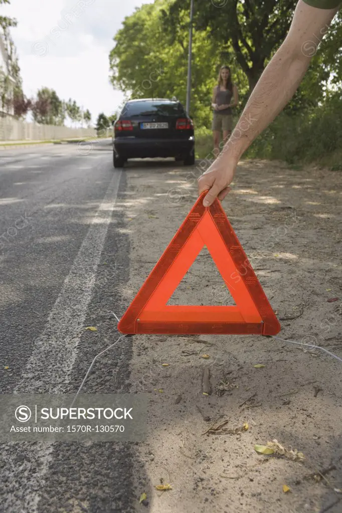 A man placing a warning triangle behind a broken down car