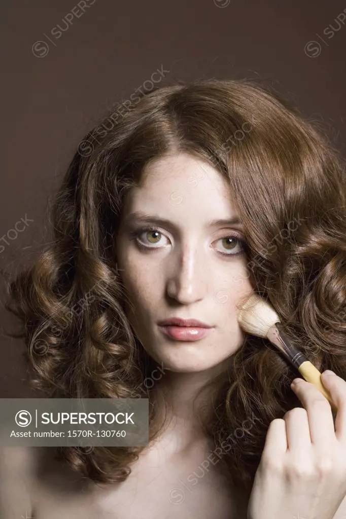 Portrait of a young woman applying face powder, 