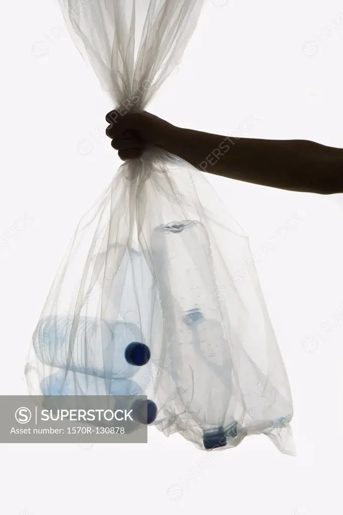 A human hand holding a transparent garbage bag of plastic bottles