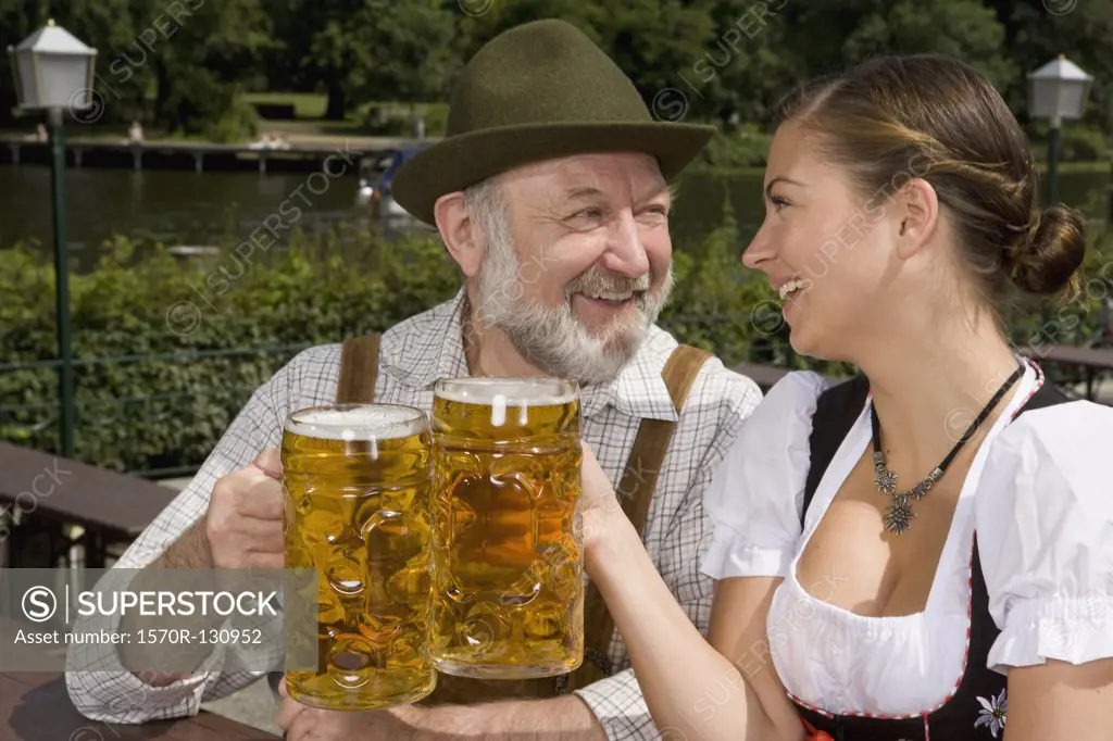 A traditionally clothed German man and woman in a beer garden toasting glasses