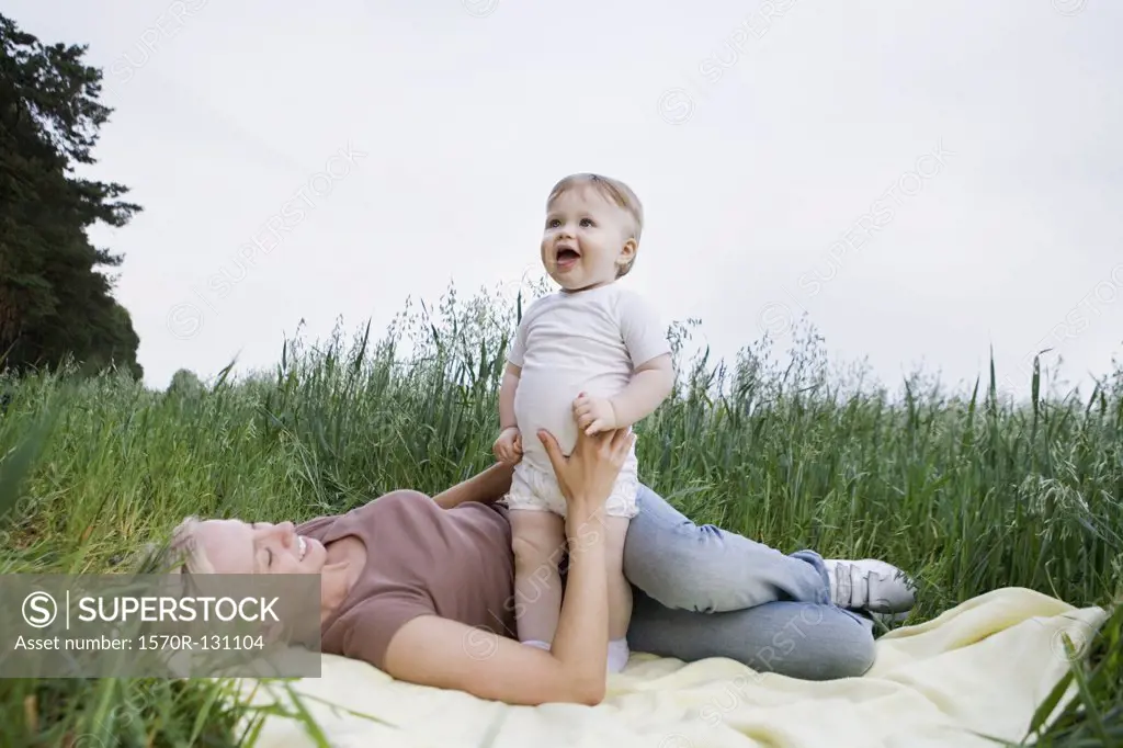 A mother and baby daughter playing on a rug in a field