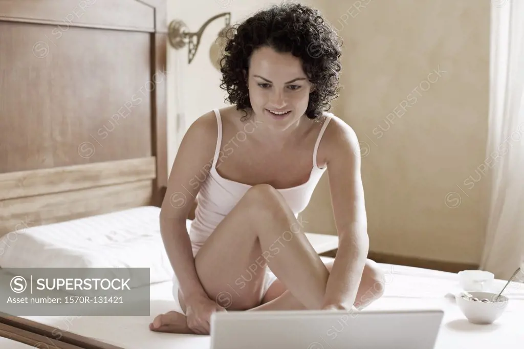 A woman sitting on her bed and using her laptop