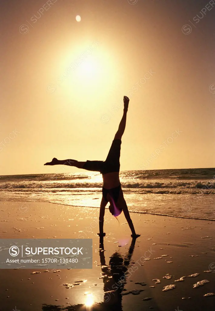 A woman doing a cartwheel on a beach at sunset