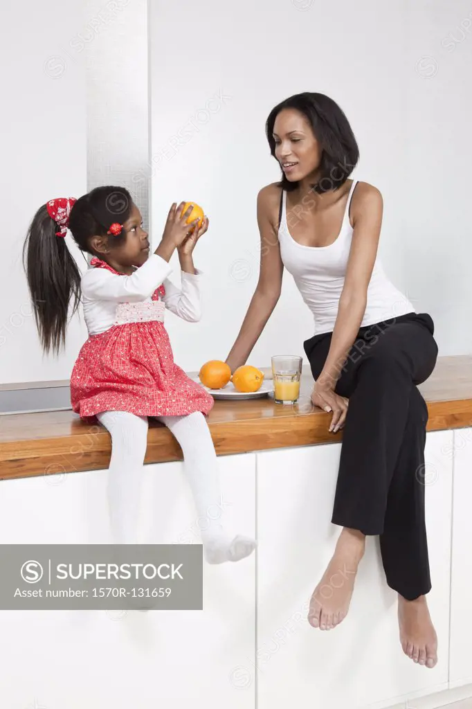 A young girl showing an orange to her mother