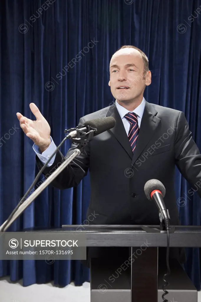 A man in a suit gesturing at a lectern