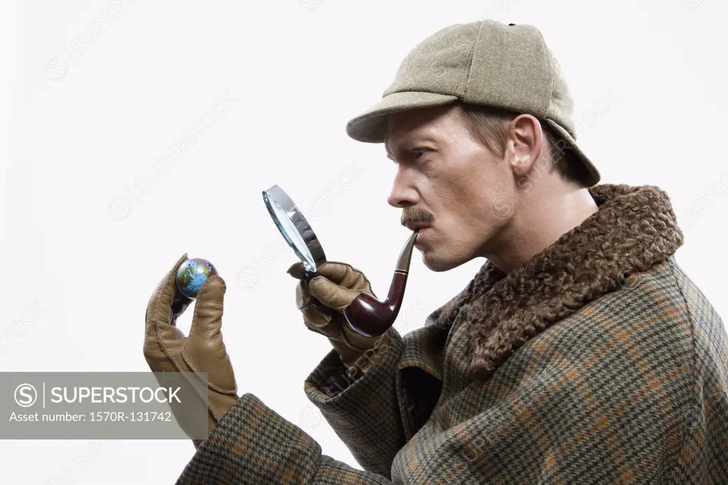 A man dressed up as Sherlock Holmes looking at a tiny globe through a magnifying glass