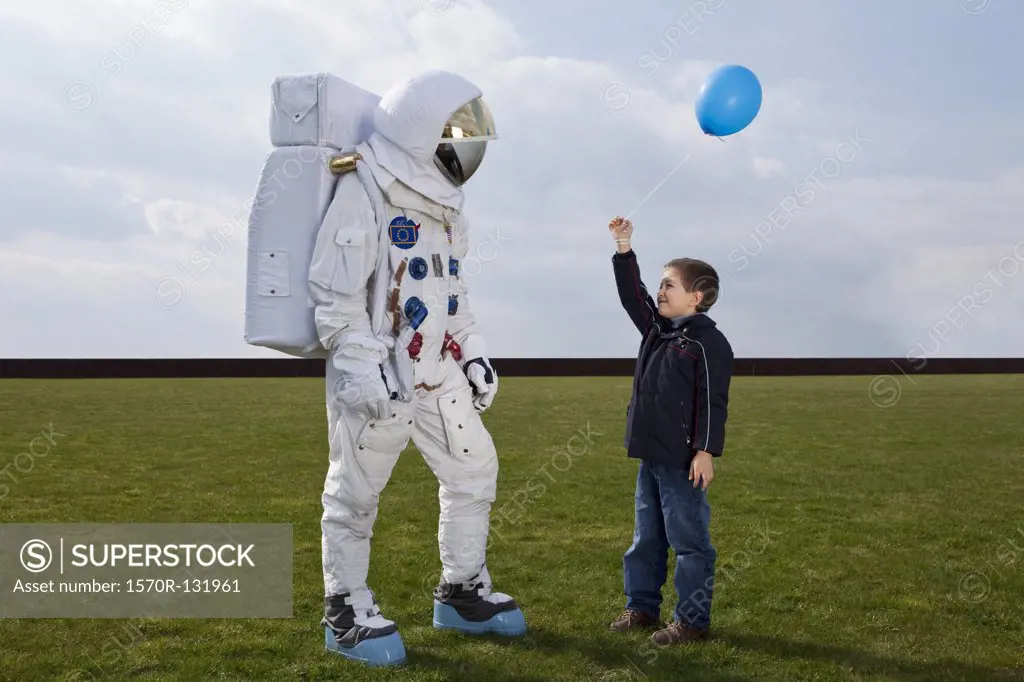 A boy holding out a balloon to an astronaut