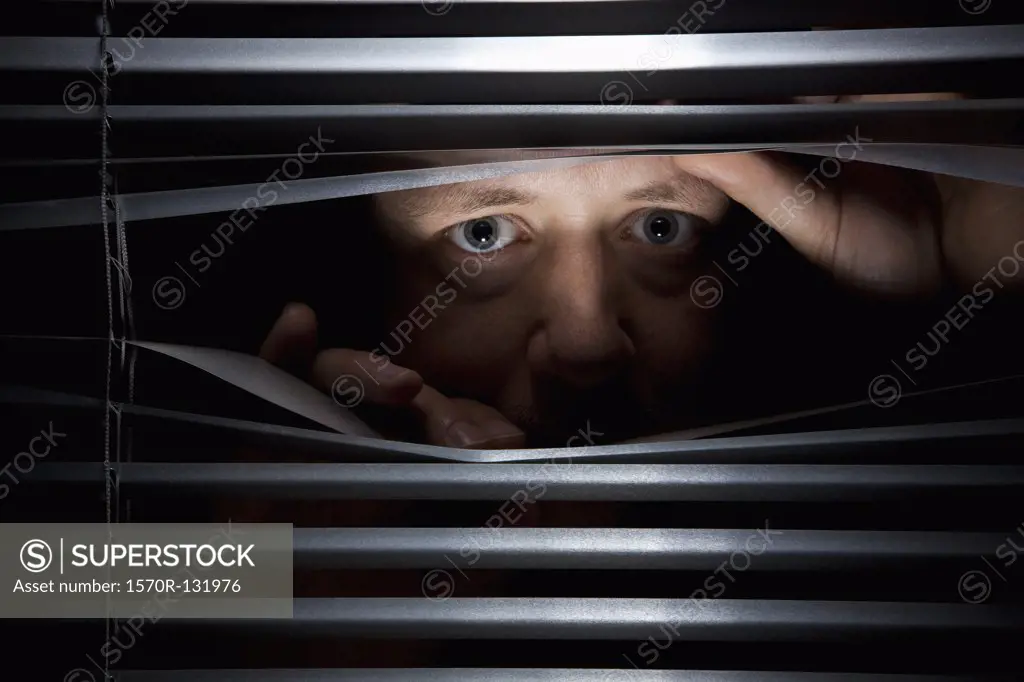 A man peeking through blinds