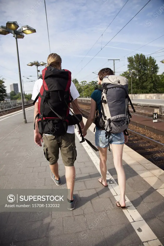 A backpacker couple walking on down a train platform