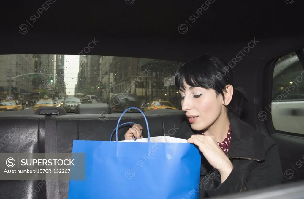 Young woman looking inside shopping bag in a taxi, New York City