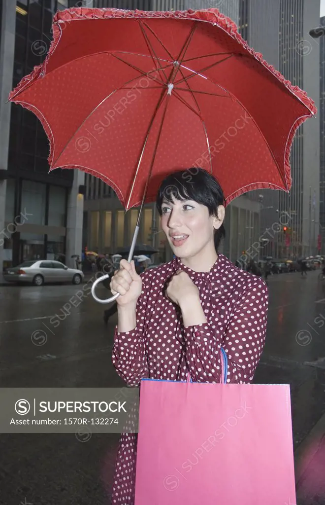 Young woman standing on street holding an umbrella and shopping bags, New York City