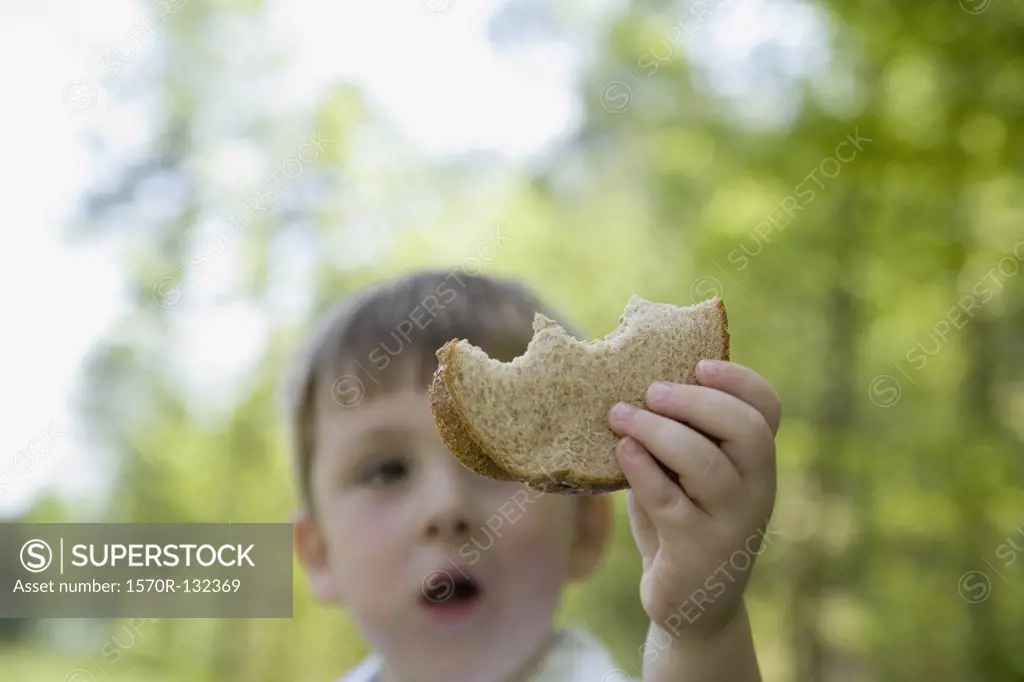 Young boy standing in park and holding slice of bread