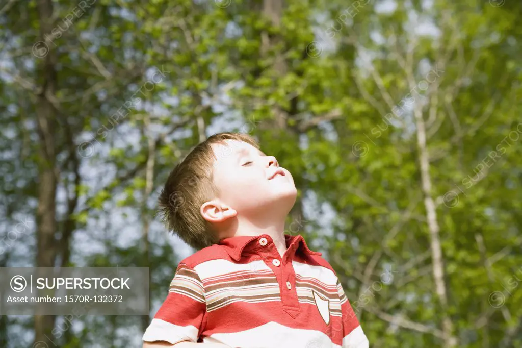 Young boy standing in park with eyes closed and head back