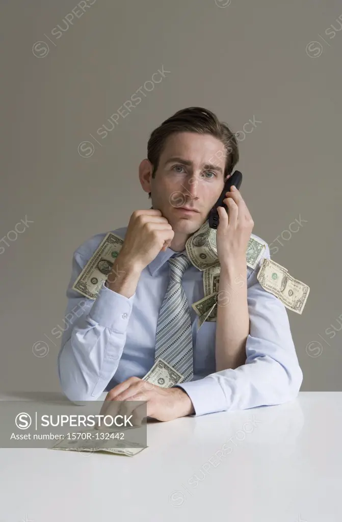 Businessman using telephone covered in money