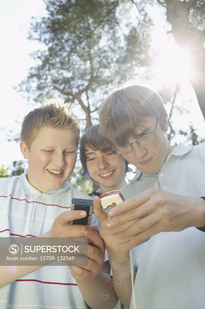 Three teenage boys huddled together using mobile phones