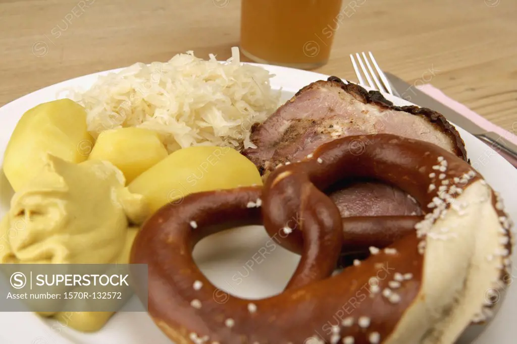 Plate with pork, sauerkraut, potato, and pretzel next to glass of beer