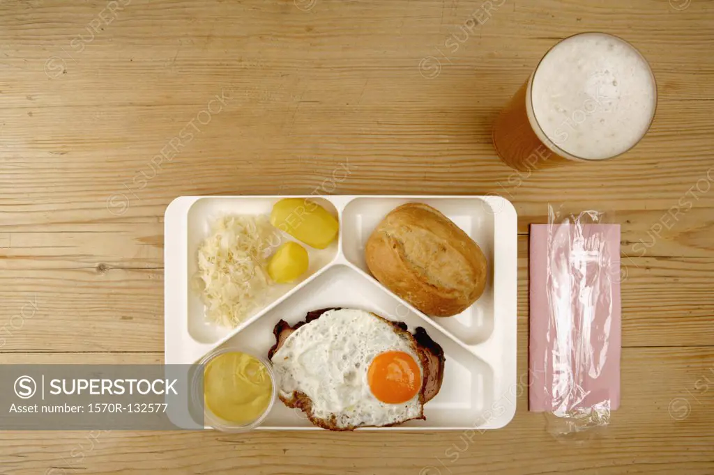 Tray with egg, sausage, sauerkraut, potato and bread next to glass of beer