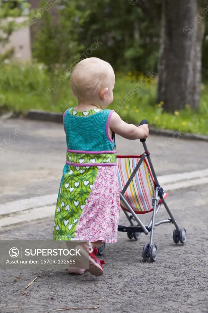 A toddler pushing a baby stroller, rear view