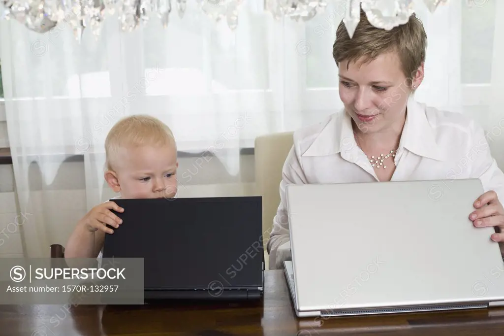 A mother and toddler opening their laptops, side by side