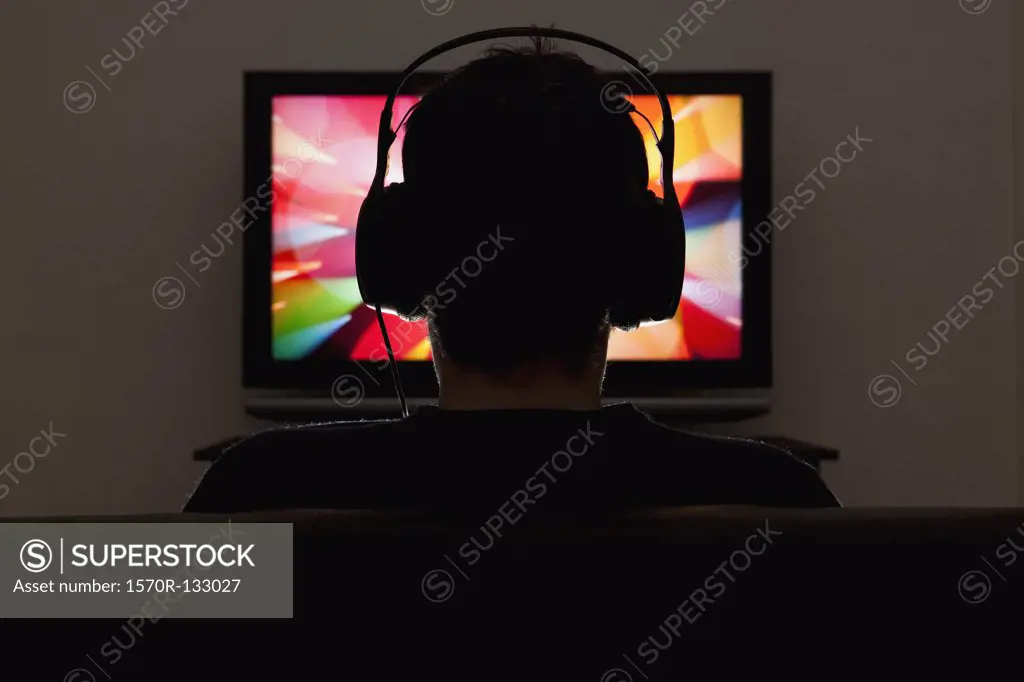 A man wearing headphones and watching television