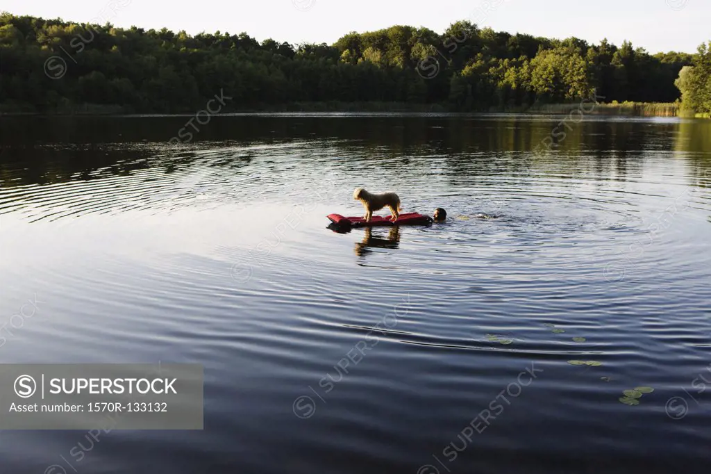 A man pushing a dog on a pool raft in a lake