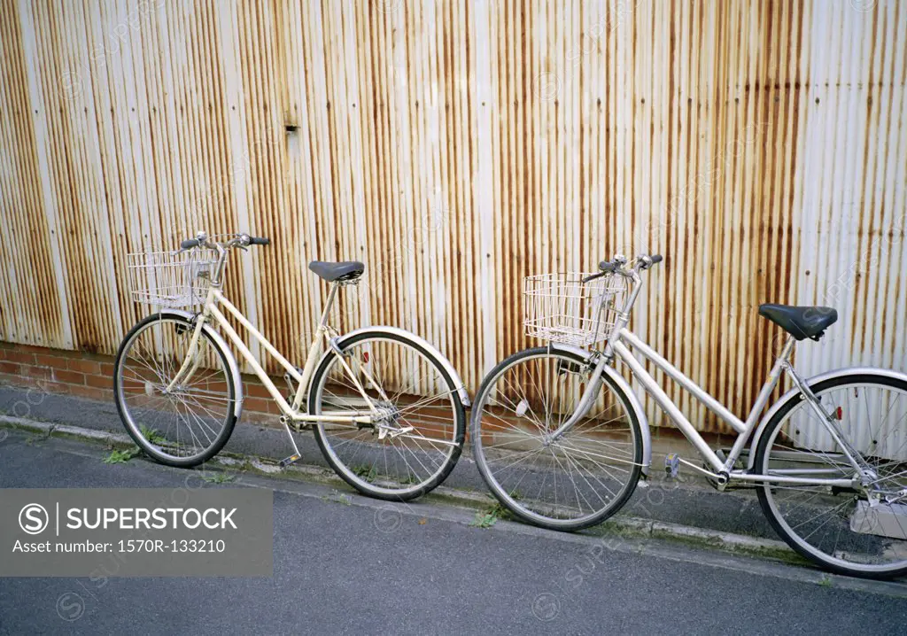 Two bicycles leaning on a wall