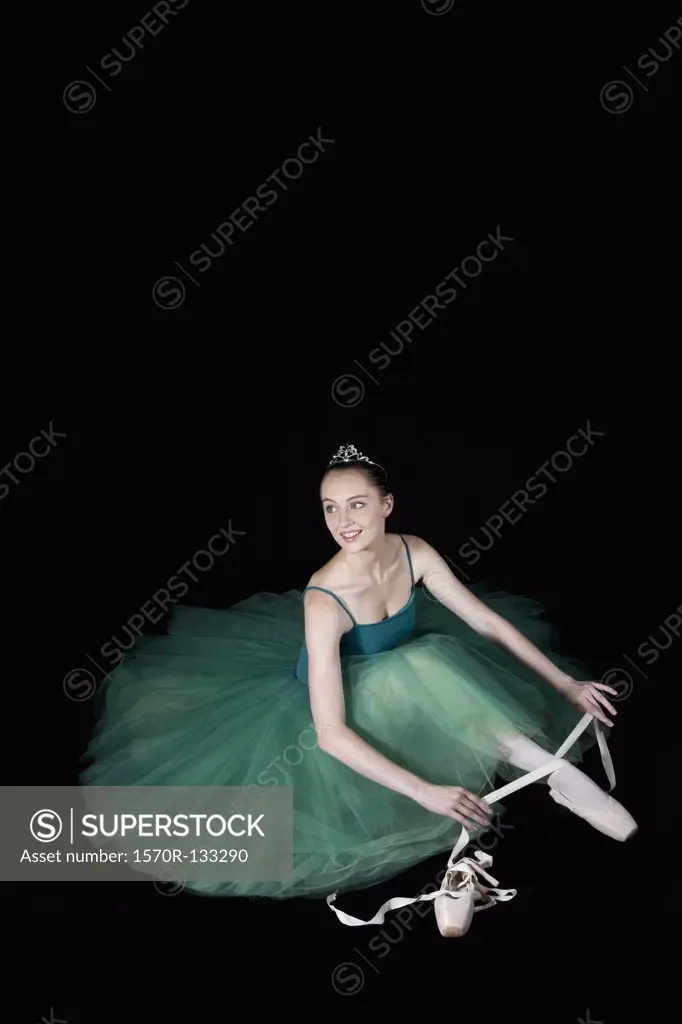 A ballet dancer wearing a costume tying her pointe shoe