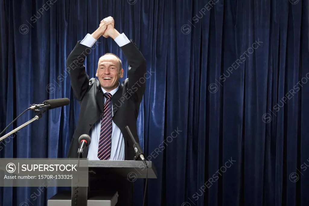 A man in a suit cheering at a lectern